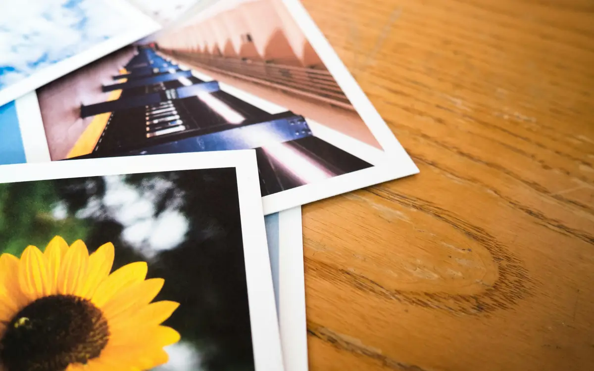 Printed photographs scattered on a wooden table, including a sunflower snapshot