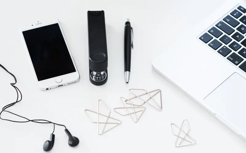Phone, earphones and laptop arranged on a white desk