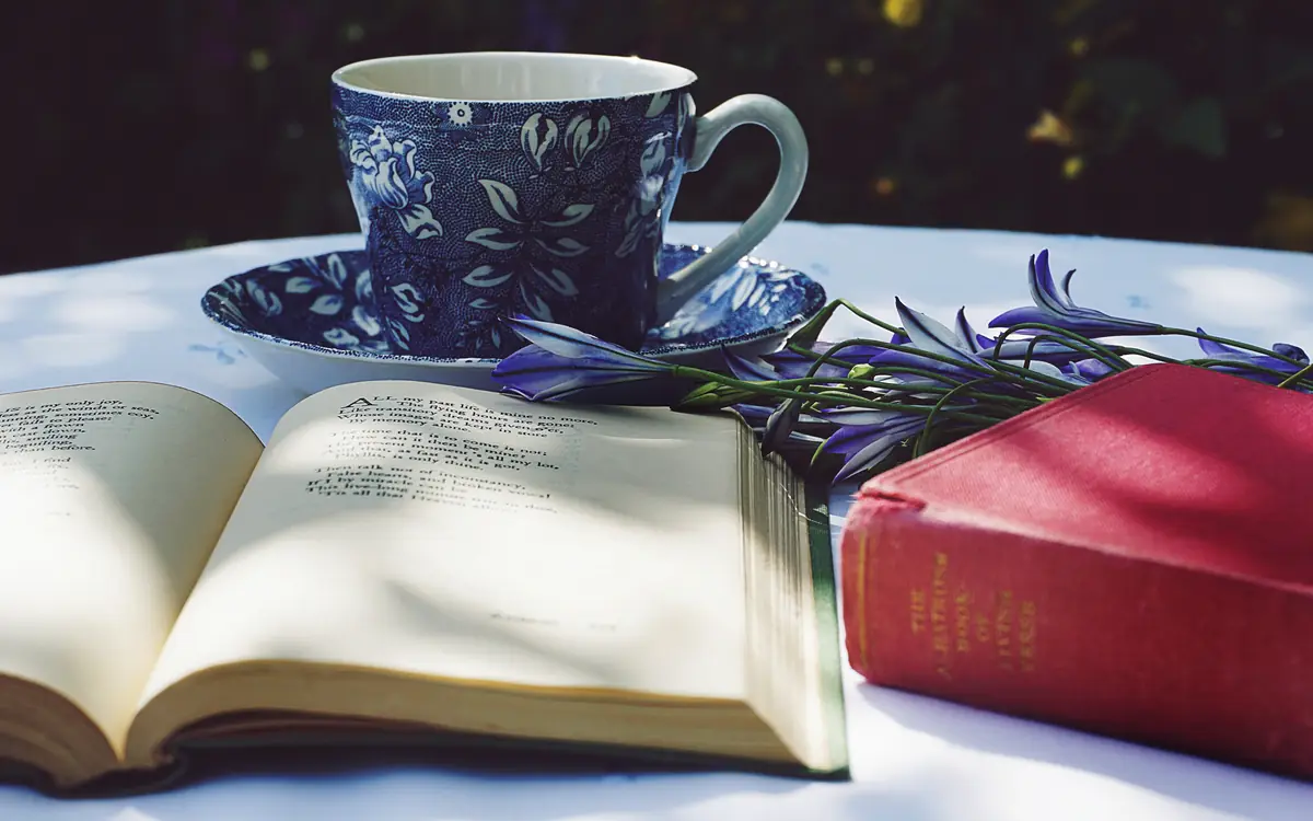 Open books beside a cup of tea and a small flower