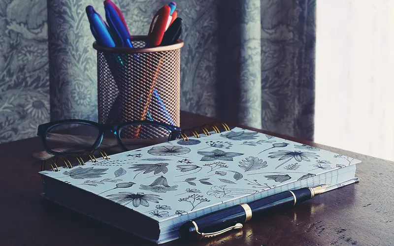 Notebook, pens and books on a wooden desk ready for editing