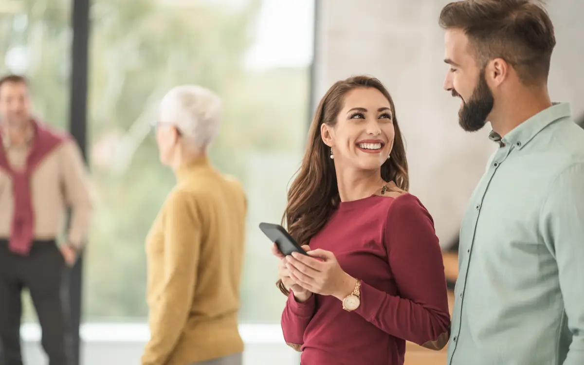 Colleagues standing together in a bright office, chatting and looking at a phone