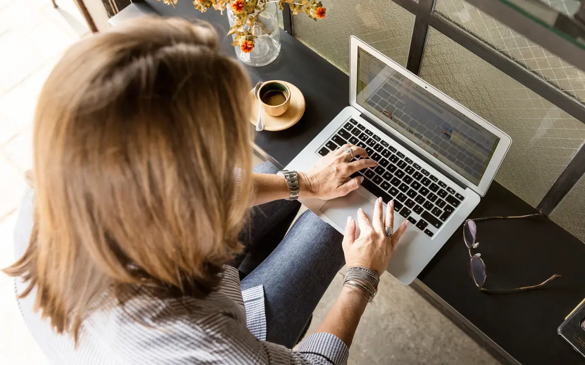 Woman typing on a laptop at a desk by a window