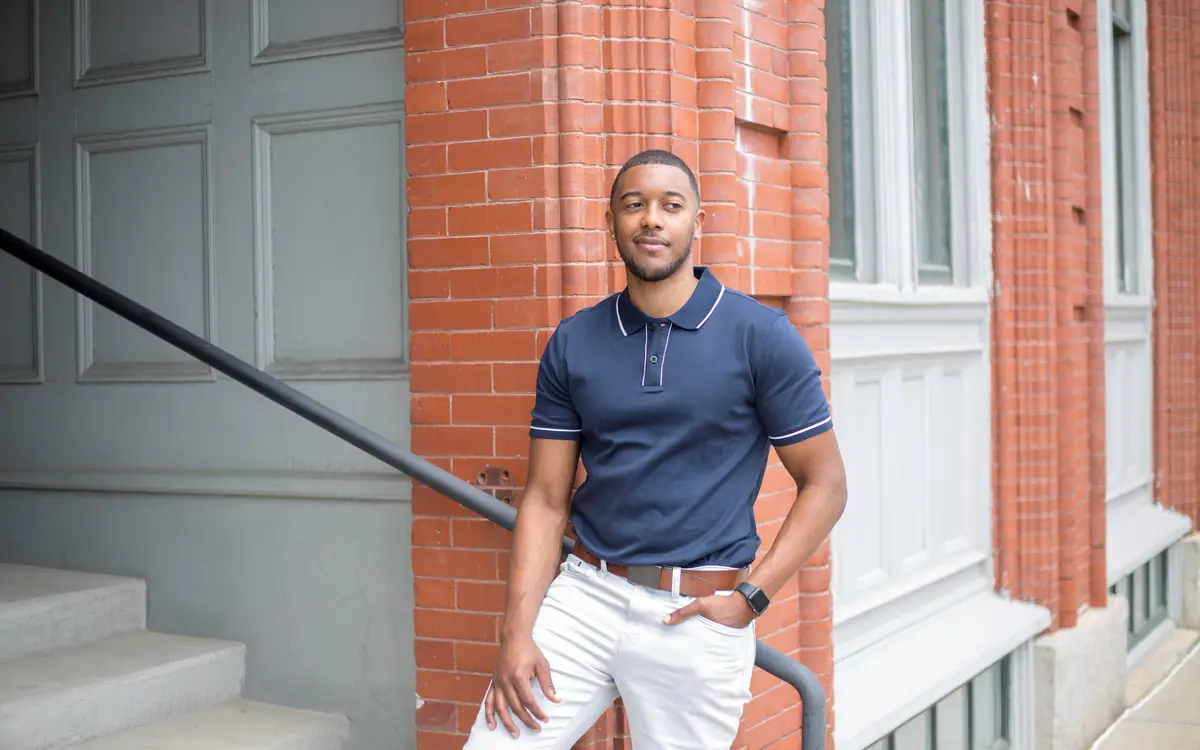 Stylish young man in a navy polo shirt posing by a brick building