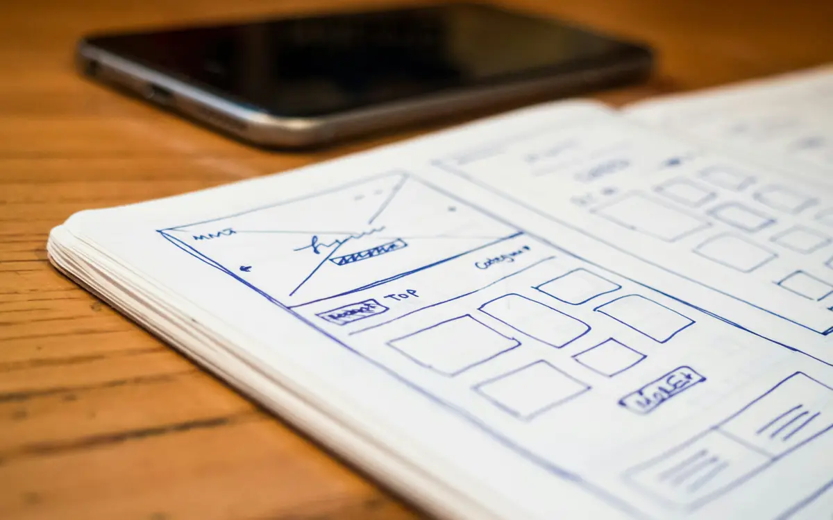 Hand-drawn website wireframe sketches on paper beside a phone