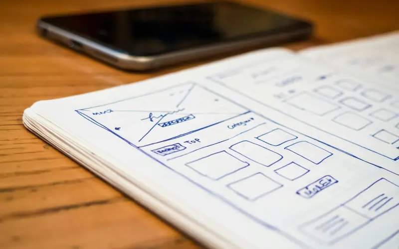Hand-drawn website wireframe sketches on paper beside a phone