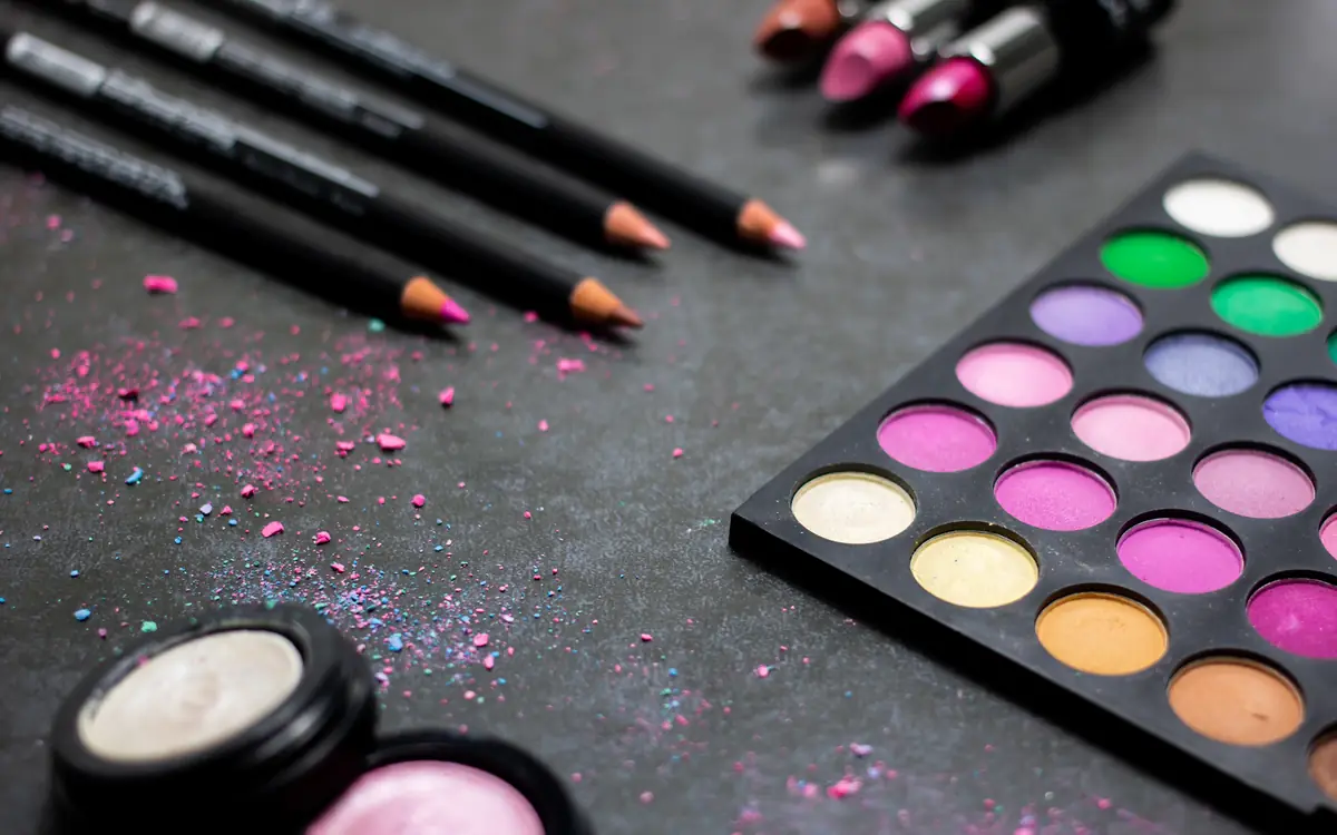 Lipsticks and a colourful eyeshadow palette on a dark surface