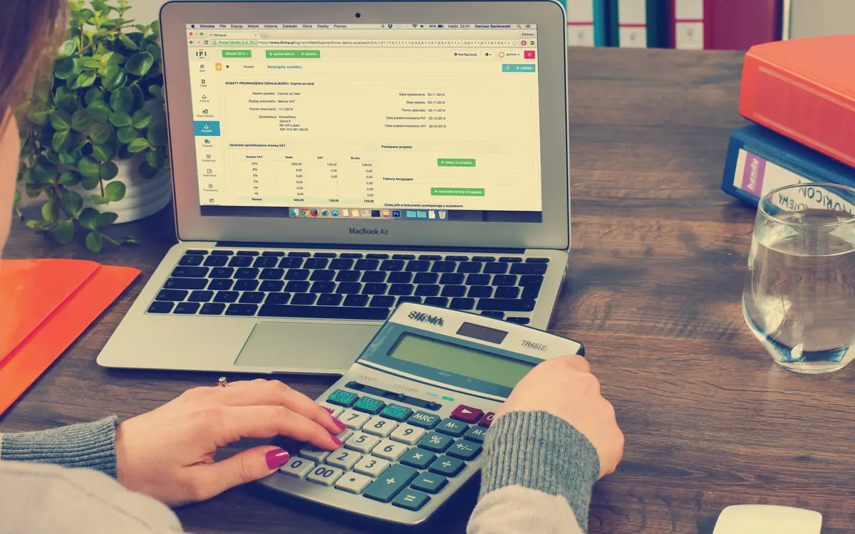 Person working with a calculator beside a laptop showing a spreadsheet