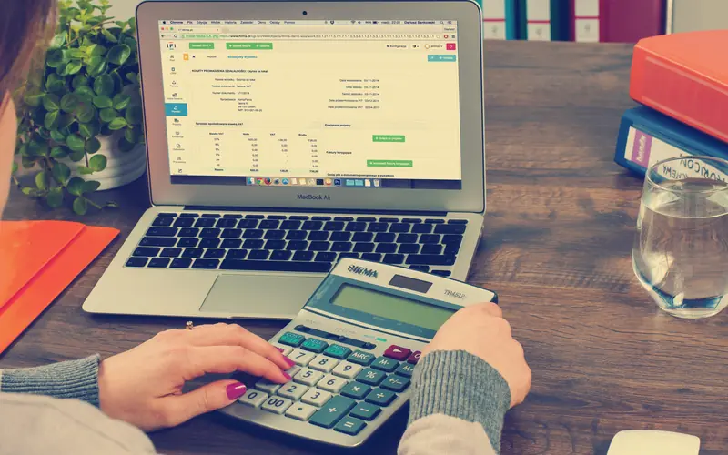 Person working with a calculator beside a laptop showing a spreadsheet