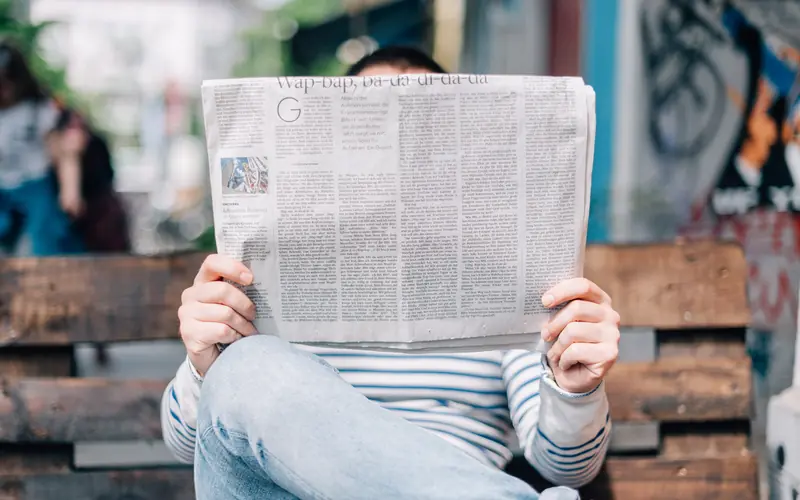 Man reading a newspaper on a bench outdoors