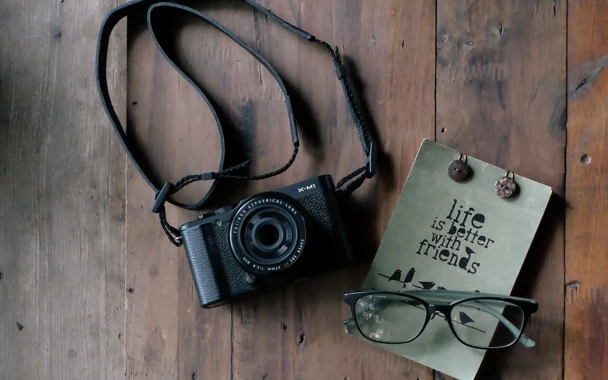 Camera with its strap beside a notebook on a wooden table