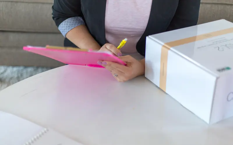 Person writing on a clipboard next to a parcel box