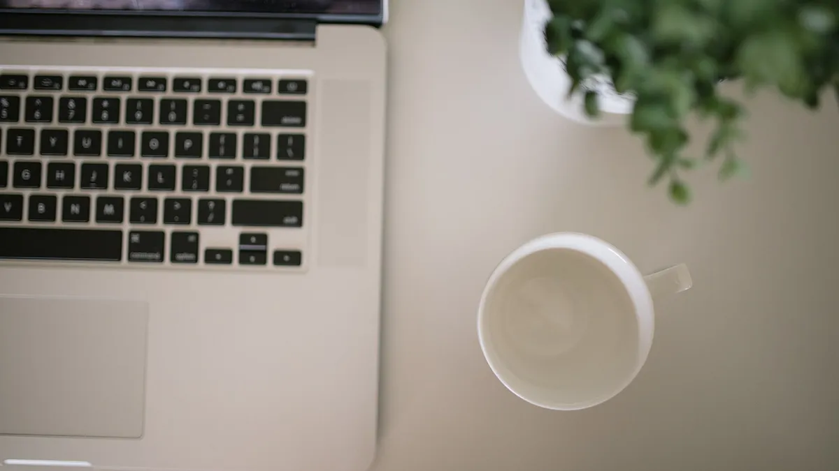 Laptop, coffee cup and a small plant on a white desk