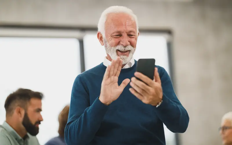 Older man smiling as he records a video on his phone in an office