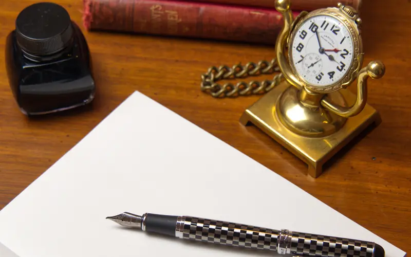 Small clock, fountain pen and paper on a writing desk