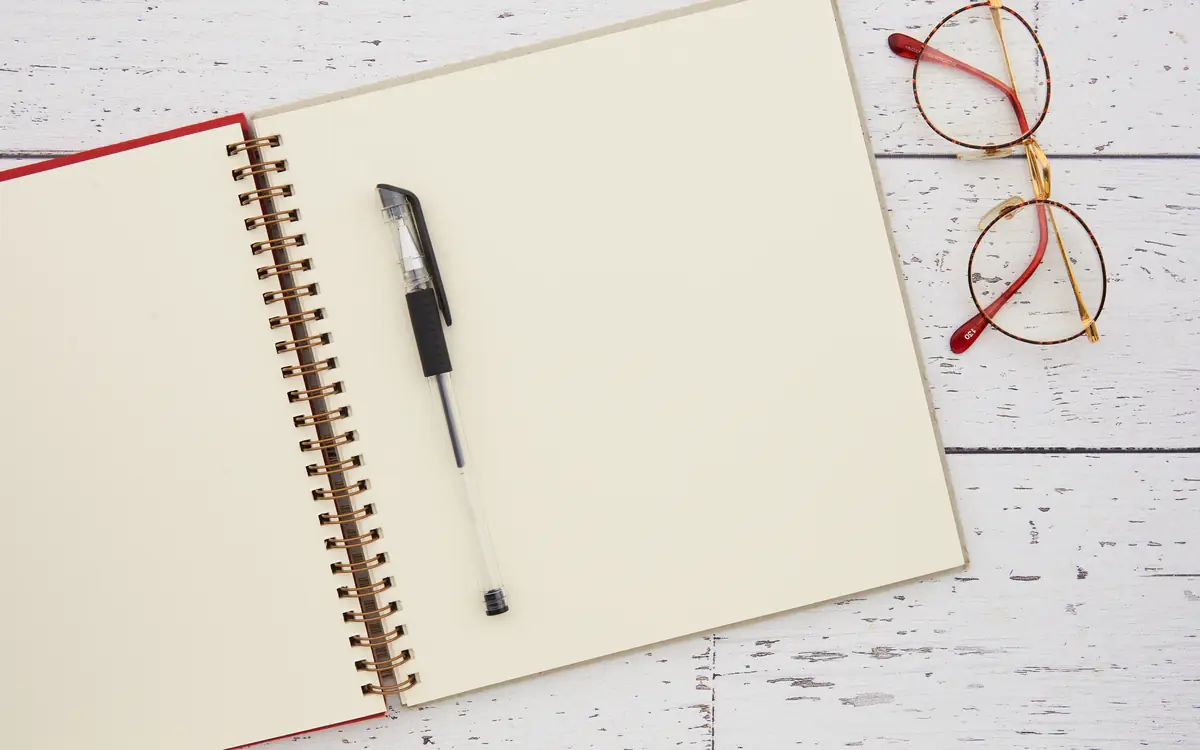 Overhead view of a blank notebook, pen and glasses on a desk