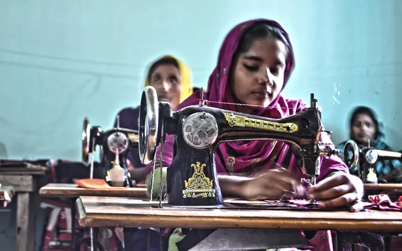 Women sewing clothes on treadle sewing machines in a workshop in Bangladesh