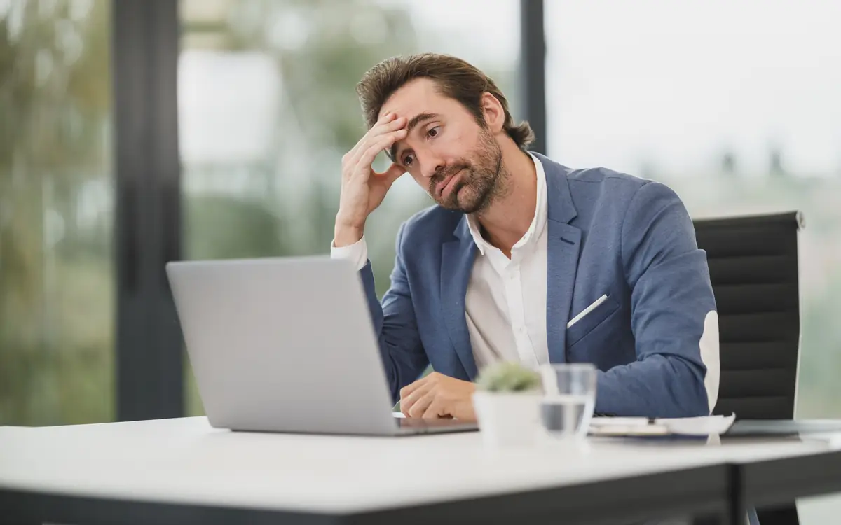 Tired man rubbing his eyes while working at a laptop in an office