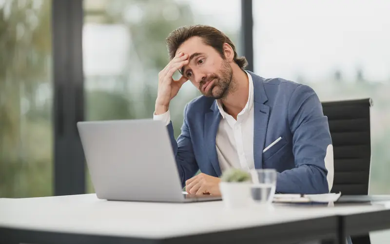 Tired man rubbing his eyes while working at a laptop in an office
